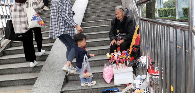 為何李奶奶會在瑞景擺攤？她的孩子去哪了呢？這些疑問一直縈繞在王媛媛心中。與奶奶相熟后，王媛媛才得知，15年前，李秋花和老伴姜水保從 江西撫州東鄉縣來到廈門，以賣冰糖葫蘆為生。5年前，老伴的支氣管炎惡化，失去了工作能力。42歲的兒子又在3年前查出腦瘤，為了治病，奶奶賣掉了老家的房子。如今，兒子一家靠兒媳賣豬肉貼補家用，還要供15歲的孫女讀中學。